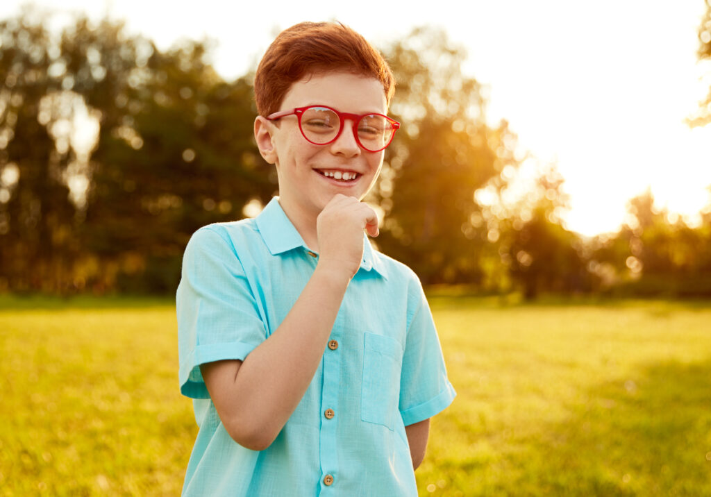 Happy kid in glasses standing on green meadow